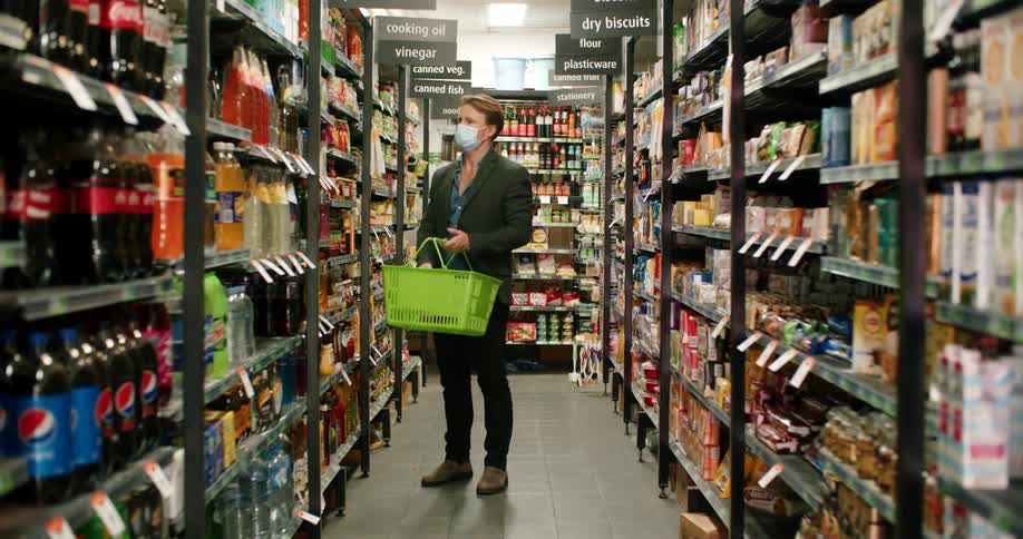 A man retrieves a bottle from a shelf in the beverage aisle of a supermarket and places it in his handheld shopping basket