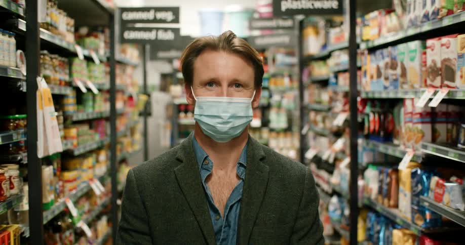 A man poses with a face mask on while standing in the aisle of a convenience store