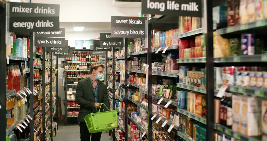 A man with a mask walking in a supermarket holding a basket