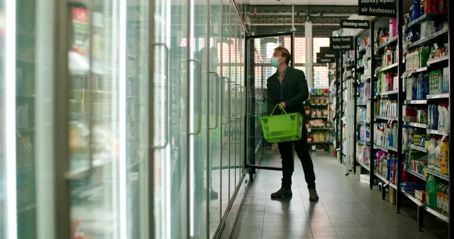A man walks down a grocery store aisle and places an item in his hand basket