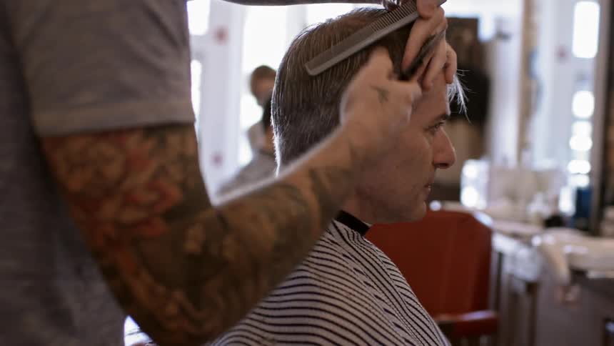 A tattooed man cuts another man's hair