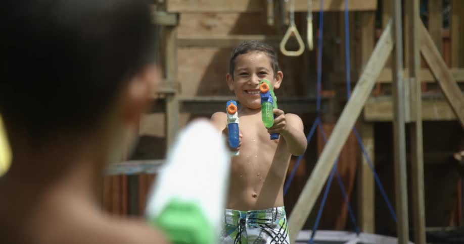 Two young shirtless boys playing with water squirt guns in the backyard