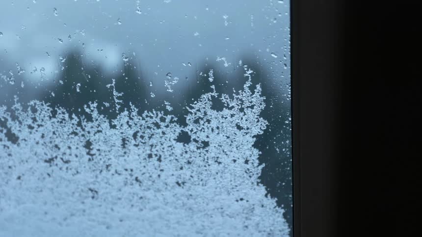 Snowflakes piling up on the surface of a window in a house during a snow storm