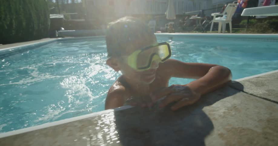 Boy wearing yellow goggles swimming in a pool in the backyard at daytime
