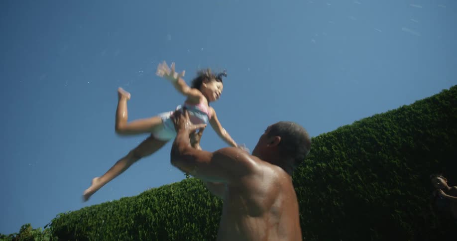 A father throwing his daughter into the air in a pool