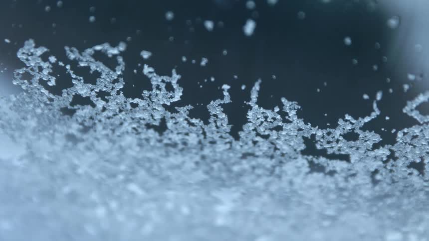 Small pieces of ice fall onto a piece of glass and slowly slide downward
