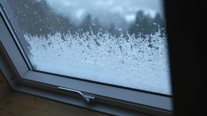 Ice crystals slowly slide down the outside of a window building a snowy landscape
