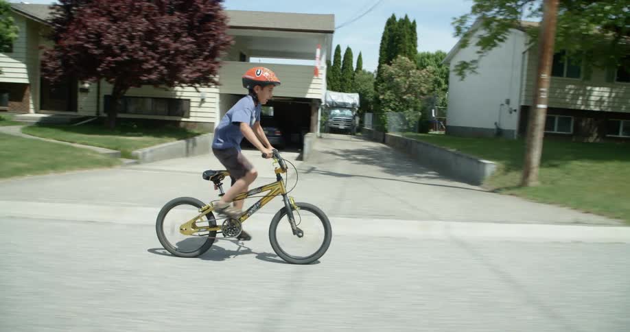 A boy stands up to pedal his bike faster as he rides past homes and lawns in a neighborhood