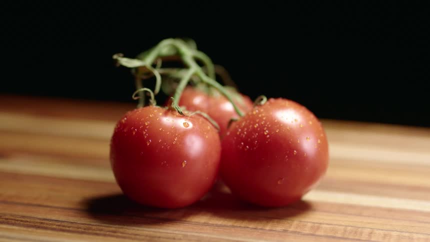 A bunch of bright red tomatoes over a wooden board in a studio