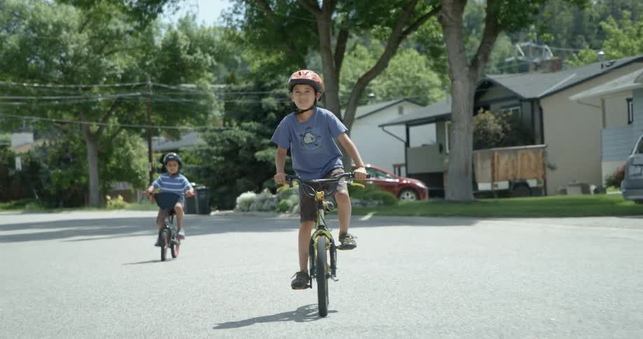 Two boys ride their bicycles down the street together
