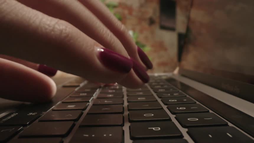 Close up of a womans fingers as she types on a laptop