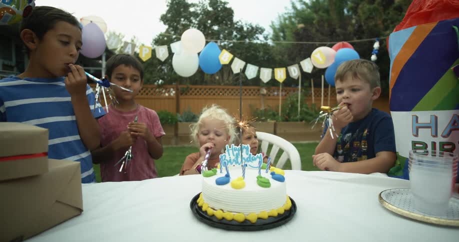 Group of children blowing party whistles in a birtday on the backyard at home