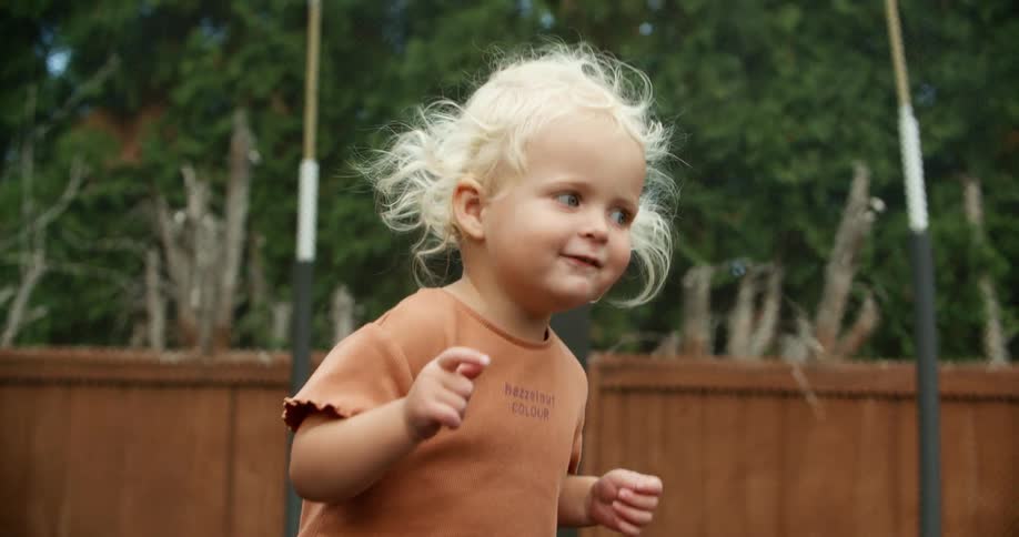 A young girl laughs while jumping on a trampoline in her backyard with a friend