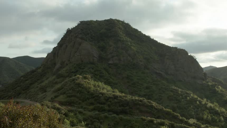 A single hill stands tall and is covered in a thick layer of green vegetation