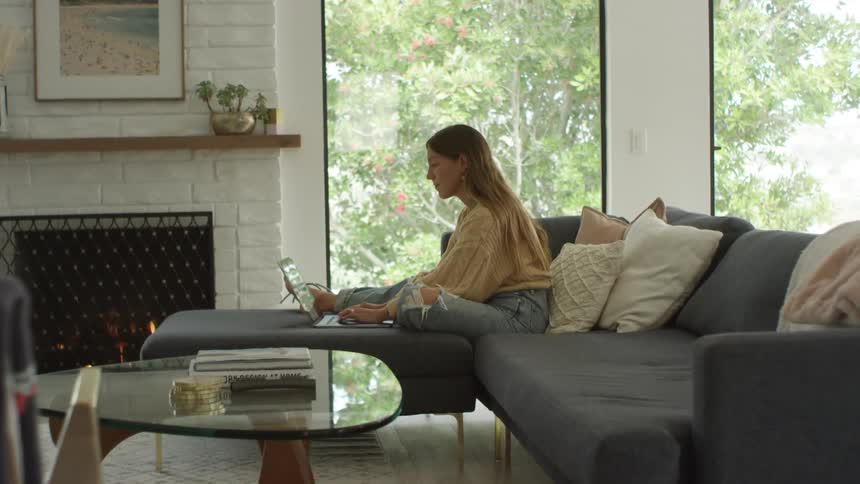 A woman is sitting on her couch typing on a laptop
