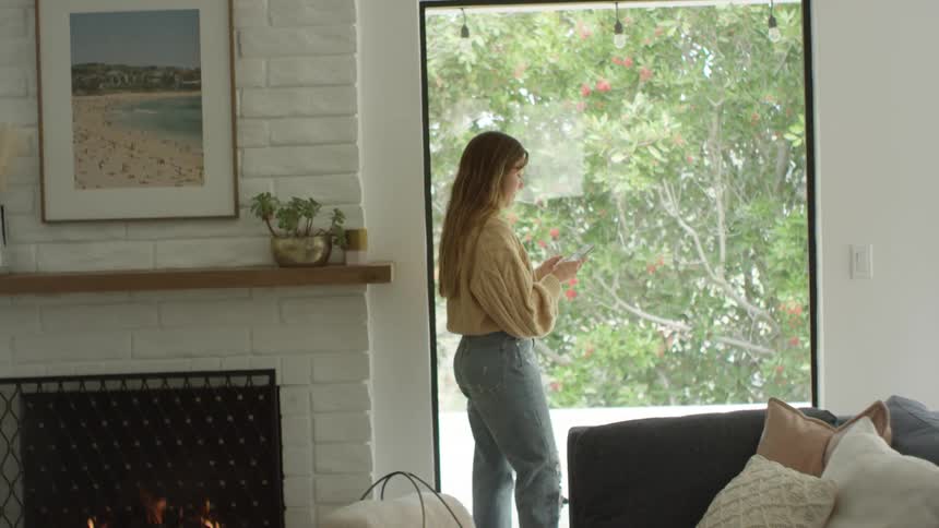 A teenage girl stands by a window at home and texts