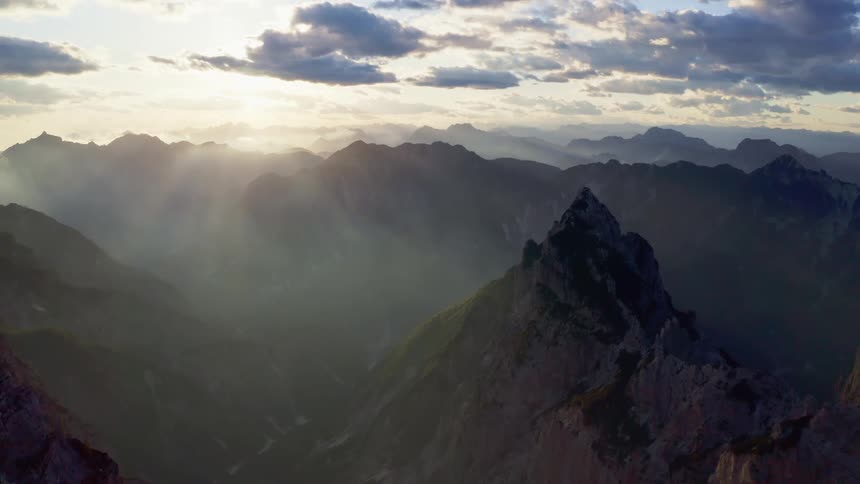 Aerial view of sunlight filtering through the fog over the snow covered steep cliffs on a mountain range at morning