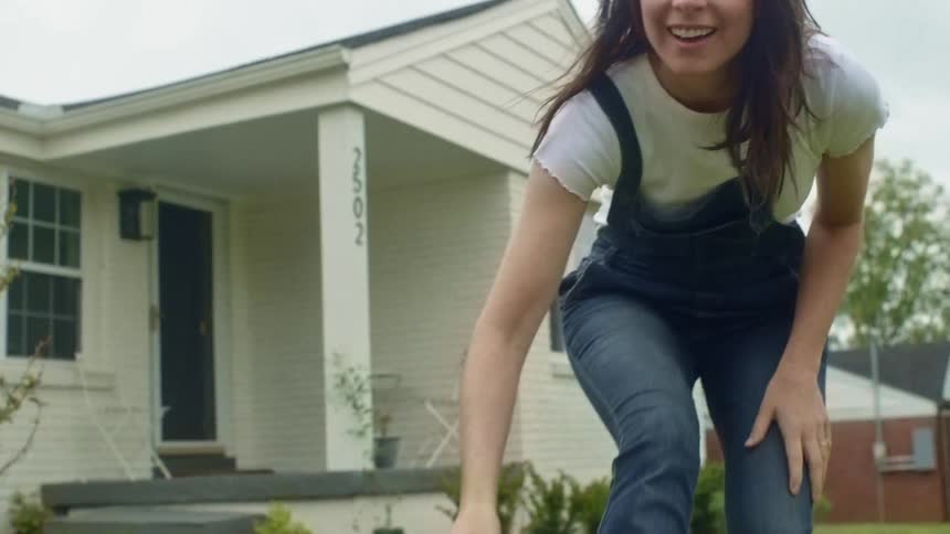 Young woman wearing jean overalls playing with her pet dog over the lawn in the front yard at home