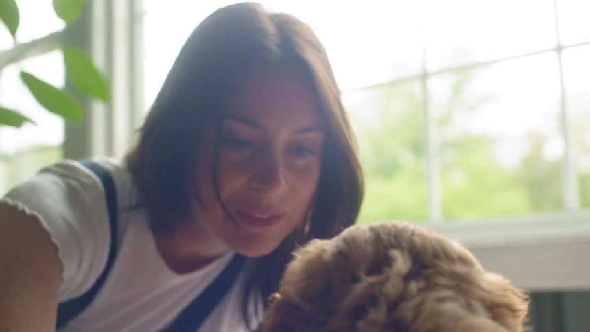 A woman petting a fluffy dog next to a window