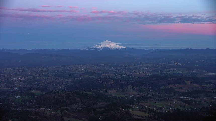 A snow capped mountain (Mount Hood) looms over a rural countryside in the evening near Portland, Oregon