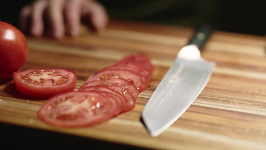 Slices of tomato and a sharp knife on a wood cutting board