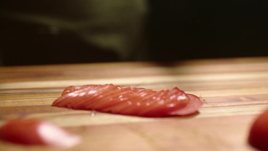 A man spreads a sliced tomato out on a wooden board