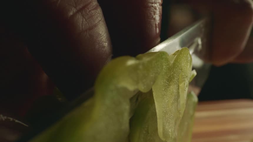 A person with a knife cutting a vegetable on a cutting board