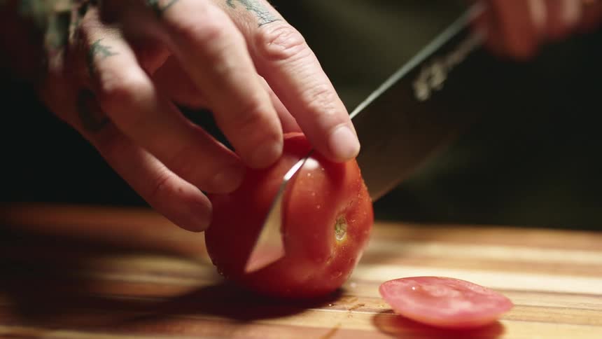 A person slicing a tomato with a knife