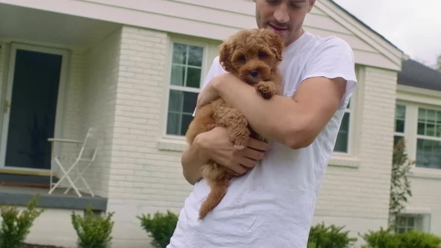 A man stands in his front yard holding a puppy dog