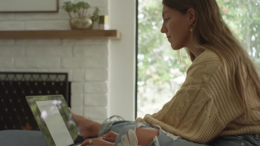A woman typing on a laptop on a couch
