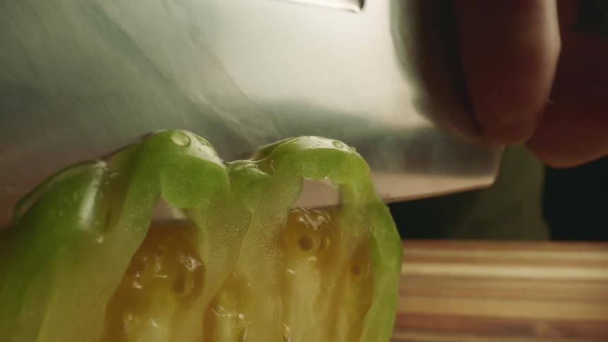 A thin slice of green tomato is cut with a very large and shiny knife