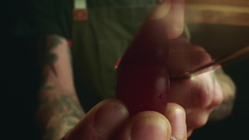 A person holding and slicing a red grape with a sharp knife