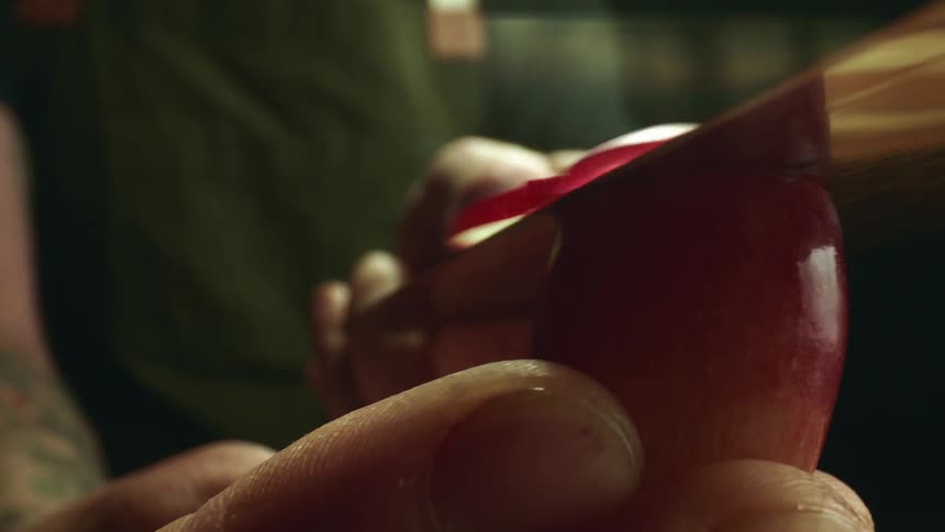 A man holds a grape in his finger as he slices it with a knife