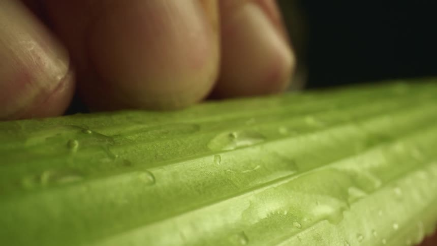 A sharp knife cutting through a piece of celery on a cutting board