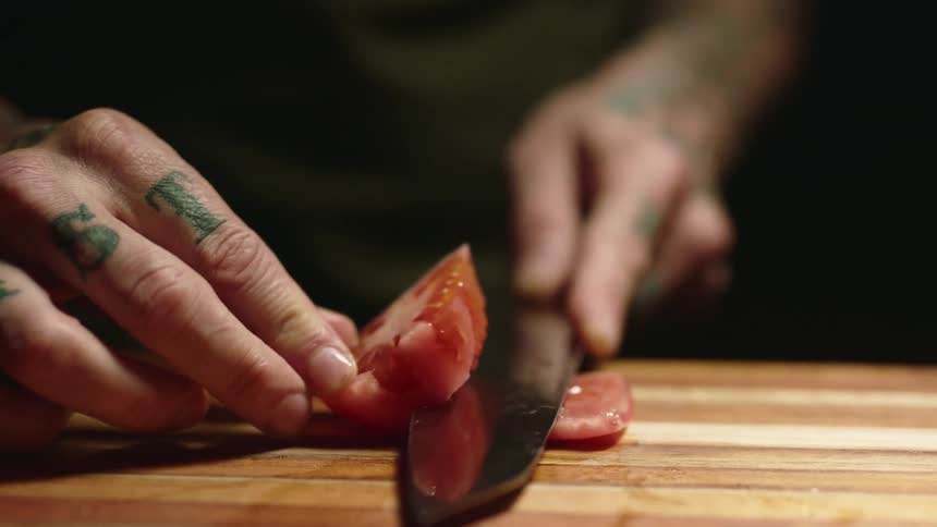A person cutting a tomato on a cutting board
