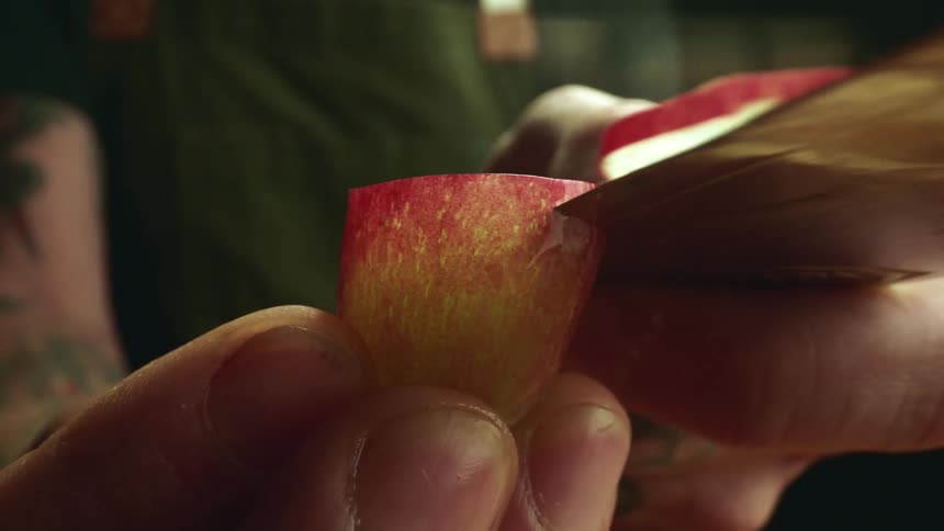 A man holds a grape in his fingers and slices it with a knife