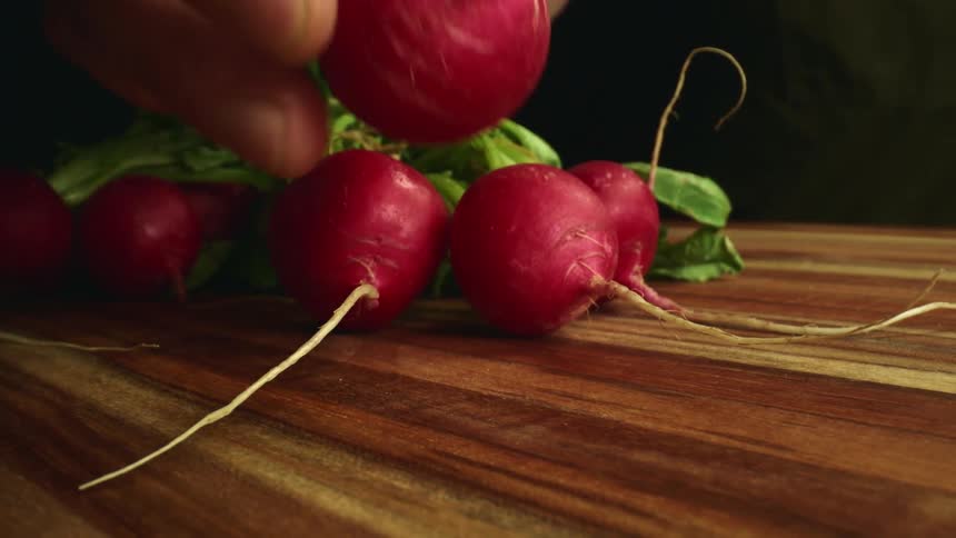A person taking a radish from a cutting board