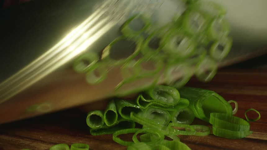 Close up of a tattoed man chopping chives with a sharp kitchen knife over a wooden board