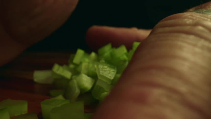 A person scooping chopped pepper and moving it
