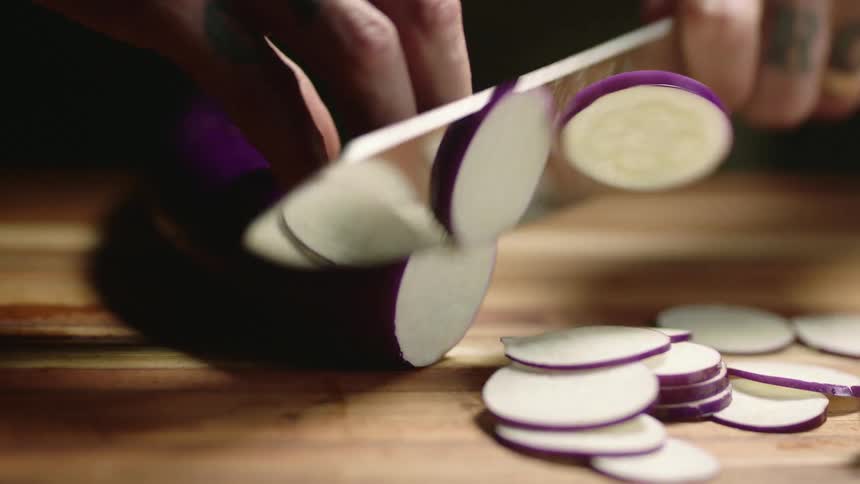 A person slicing up an eggplant on a wood cutting board