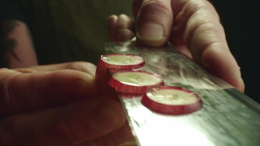Close up of a tattoed man slicing grapes with a sharp kitchen knife over a wooden board