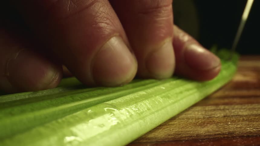 A person uses a knife to slice lengthwise along a vegetable on a wooden cutting board