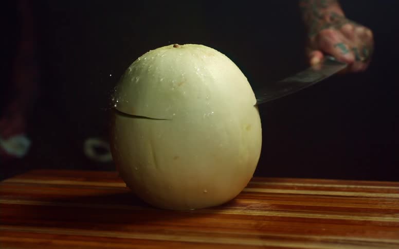 A man uses a large curved knife to slice off the top of a cantaloupe