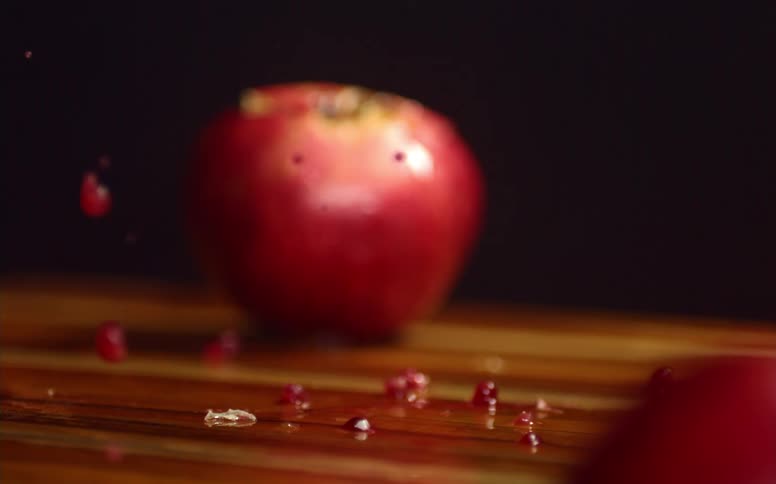 A sharp knife cutting through a pomegranate on a wood cutting board