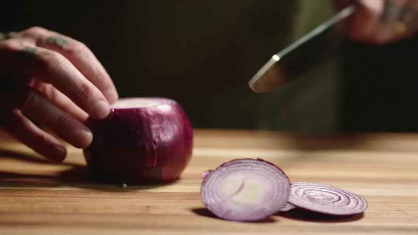 A man is cutting an onion with a knife indoors