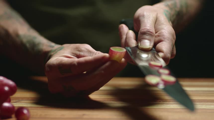 A man holds a grape and slices it with a knife