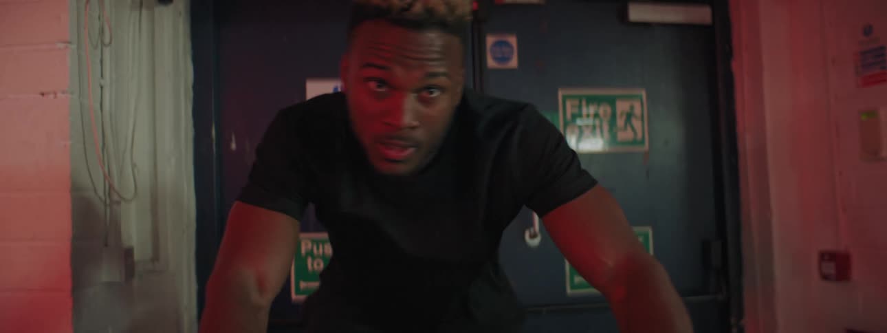 A man pedals an exercise bike quickly in a small dark room