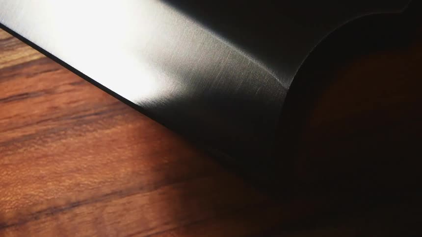 Close up of the sharp edge of a cleaver resting over a cutting board under moving white lights