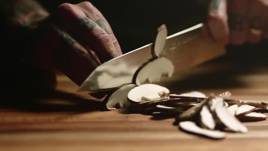A person cutting a mushroom with a knife on a cutting board