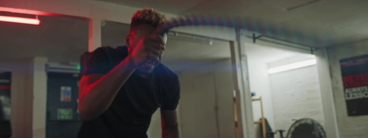 A man in a gym exercising with ropes with equipment and a door in the background